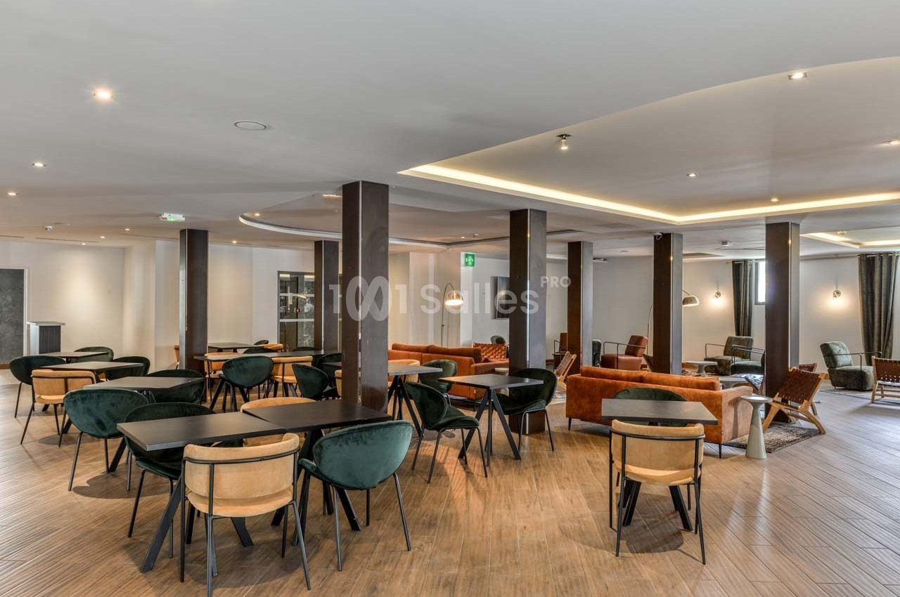 Salle spacieuse avec tables, chaises modernes et canapés, éclairée par des spots et des lumières suspendues.