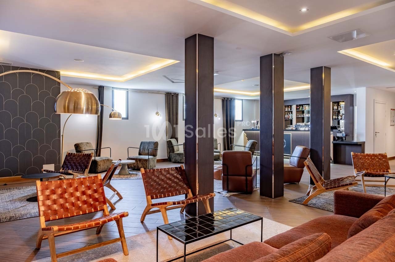 Salon moderne avec fauteuils en cuir tressé, tables basses et éclairage chaleureux, près d'un bar en arrière-plan.