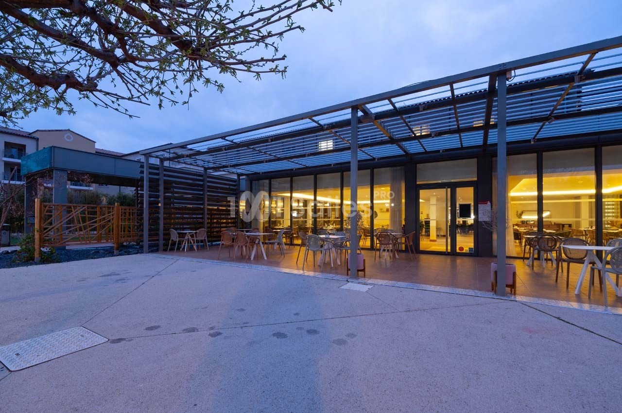 Terrasse extérieure d'un bâtiment moderne avec des tables et des chaises, éclairée à la tombée de la nuit.
