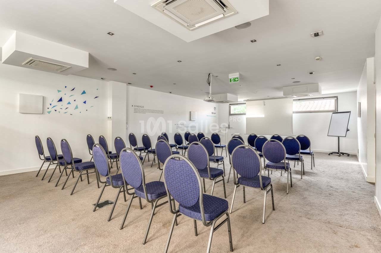 Salle de réunion lumineuse avec des chaises disposées en rangées face à un tableau blanc et un projecteur.