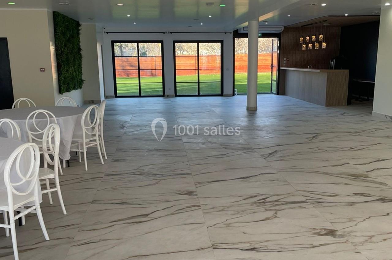 Salle lumineuse avec sol en marbre, tables blanches, chaises élégantes, bar en bois et grandes baies vitrées donnant sur un…