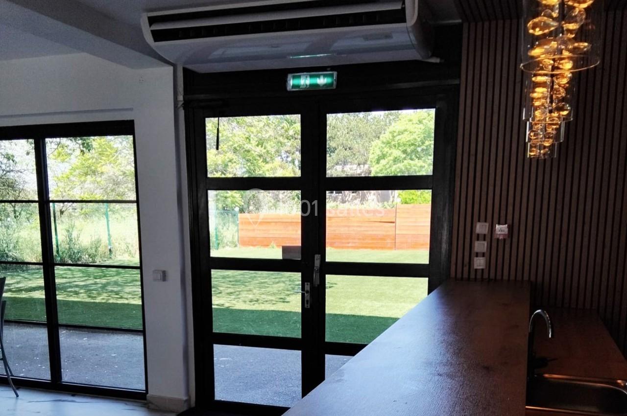 Porte vitrée donnant sur un jardin avec pelouse, vue depuis un intérieur moderne avec comptoir en bois et luminaires…
