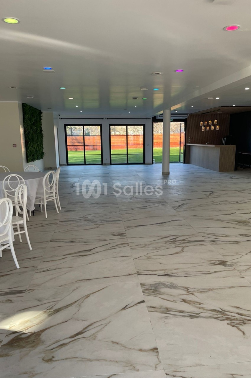 Salle lumineuse avec sol en marbre, chaises blanches, mur végétal et baies vitrées donnant sur un espace extérieur.