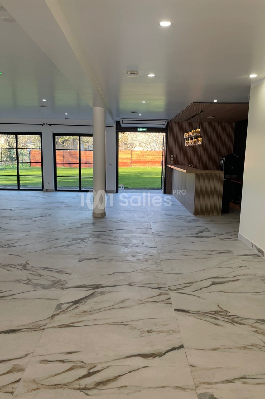 Salle lumineuse avec sol en marbre, comptoir en bois, grandes baies vitrées donnant sur un espace extérieur verdoyant.