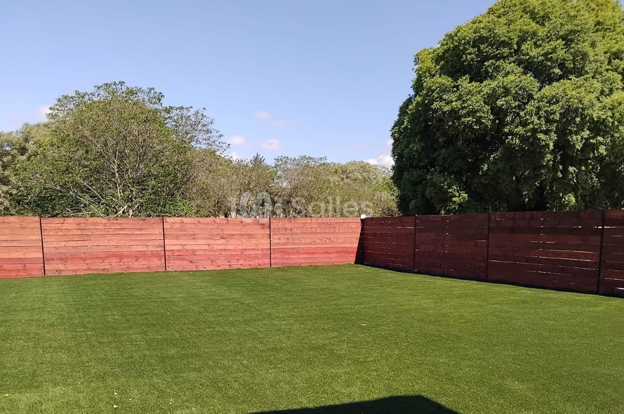 Pelouse verte bien entretenue entourée de clôtures en bois rouge et d'arbres sous un ciel dégagé.