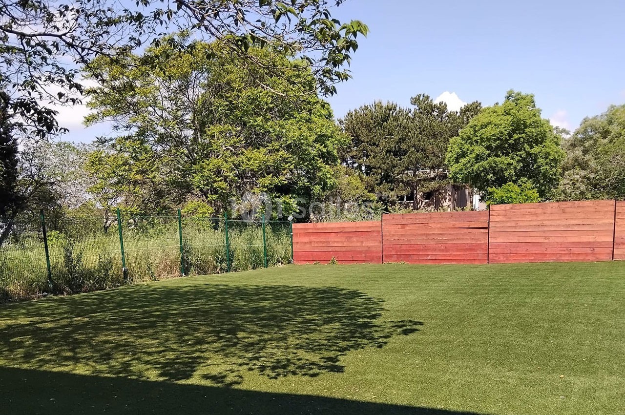 Pelouse verte bordée d'une clôture en bois rouge et d'arbres sous un ciel dégagé.