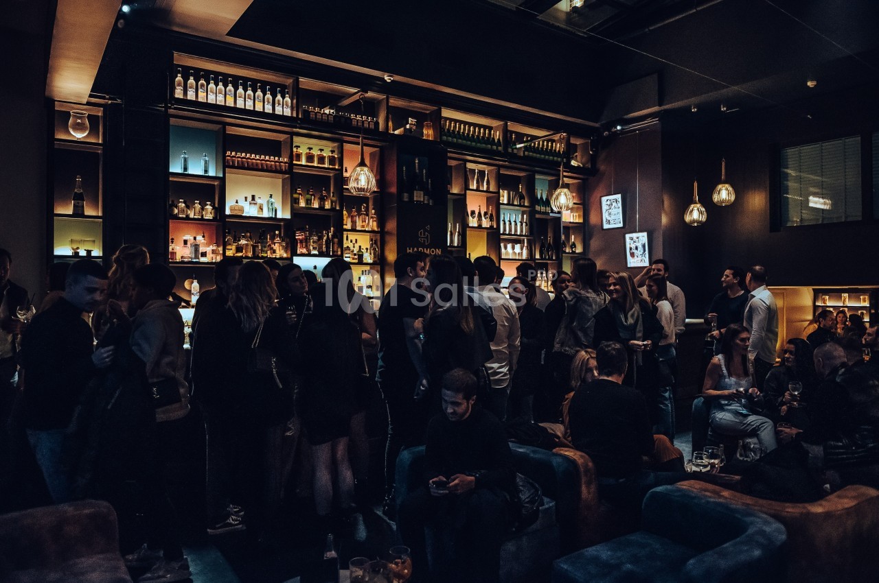 Groupe de personnes rassemblées dans un bar à l'ambiance tamisée, avec des étagères remplies de bouteilles en arrière-plan.