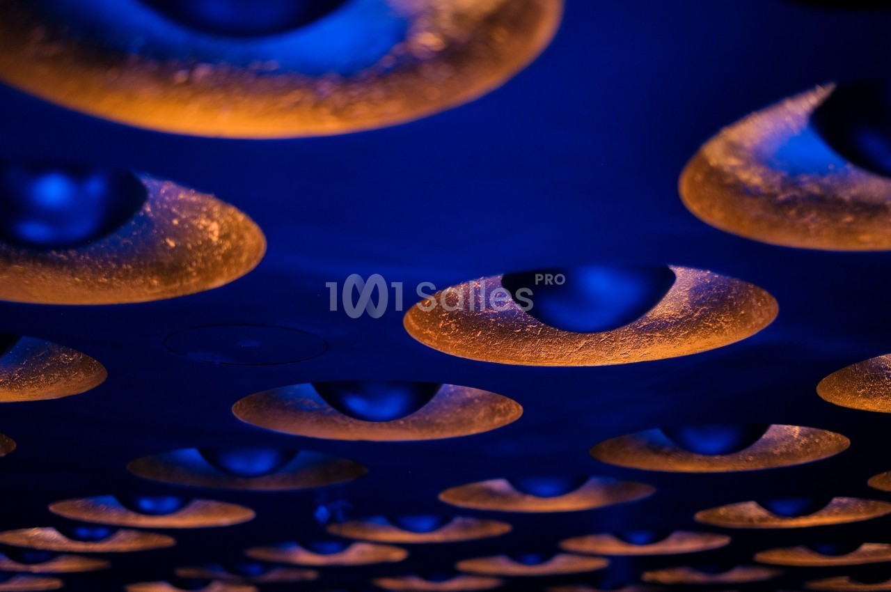 Plafond avec des luminaires circulaires émettant une lumière orange, contrastant avec un éclairage bleu.