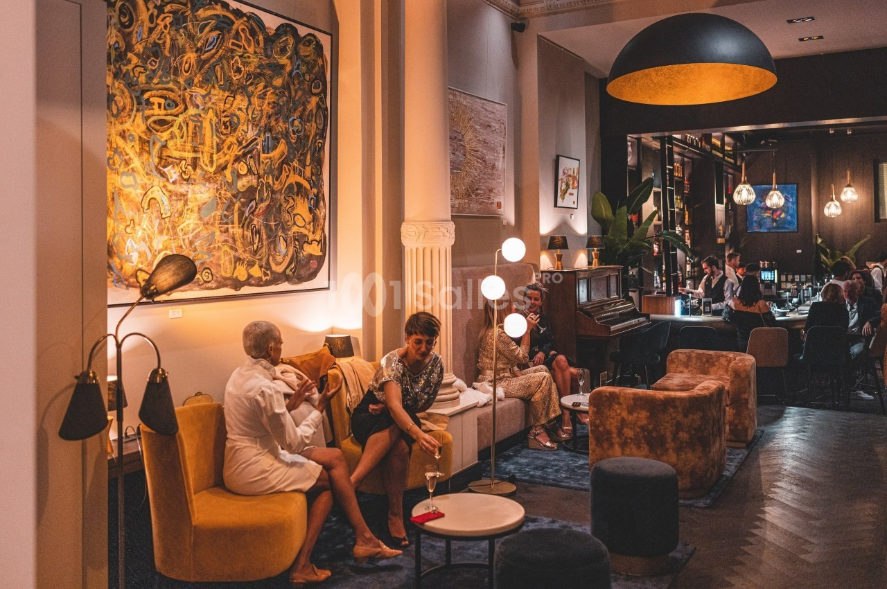 Salon chaleureux avec canapés, œuvres d'art au mur, éclairage tamisé et personnes discutant autour de tables.