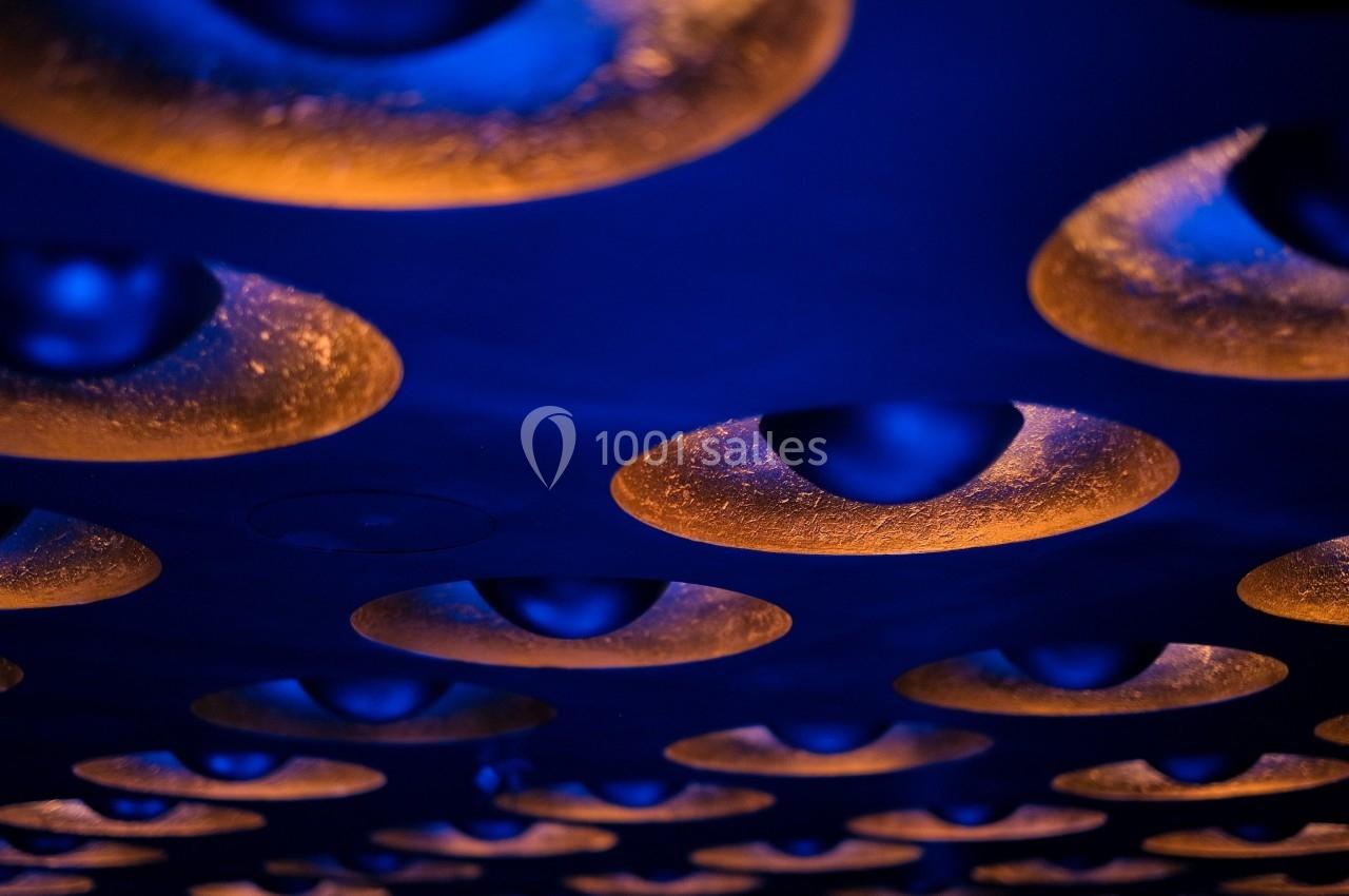 Plafond avec des luminaires circulaires encastrés diffusant une lumière orange sur un fond bleu sombre.