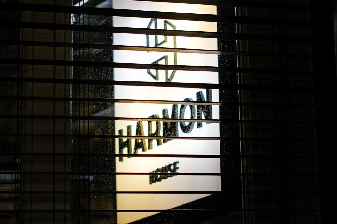 Panneau lumineux avec le logo et le texte ’Harmon’ visible à travers des stores en métal.