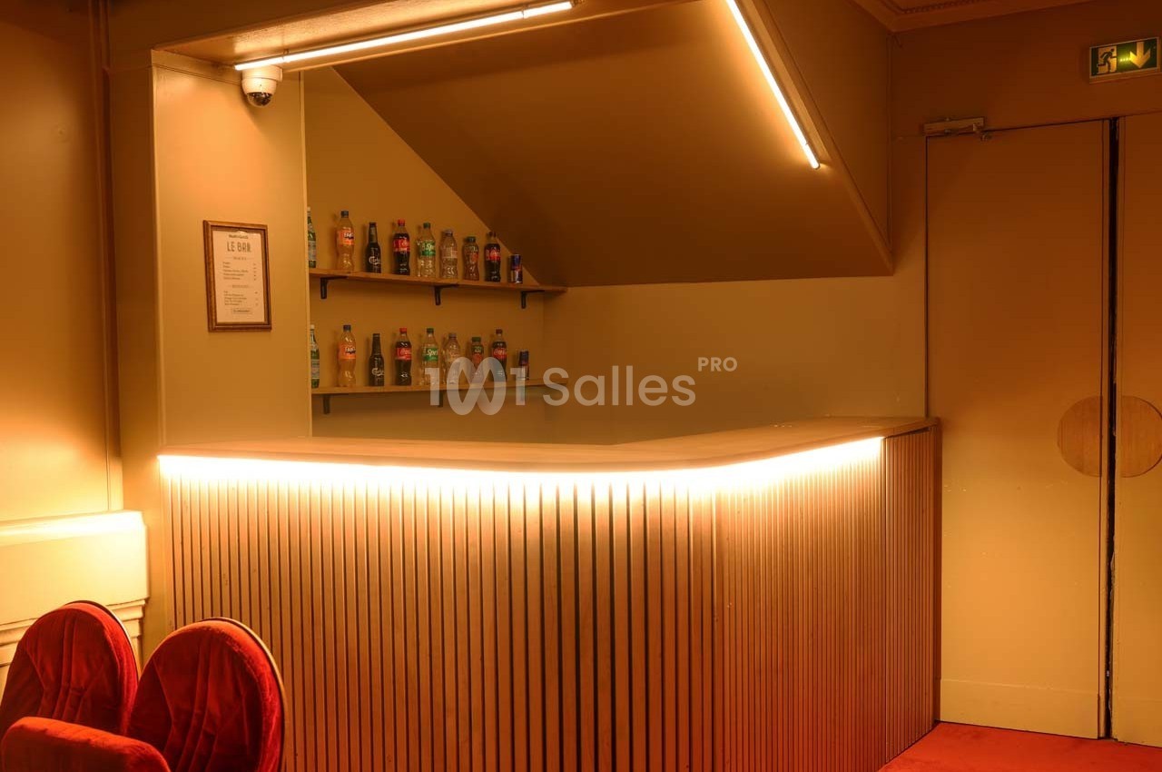 Comptoir de bar en bois éclairé, avec étagères contenant des bouteilles, dans un intérieur au ton chaleureux.
