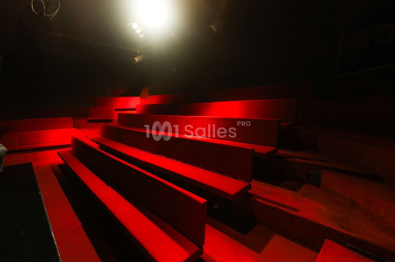 Gradins vides en velours rouge éclairés par une lumière vive dans une salle sombre.