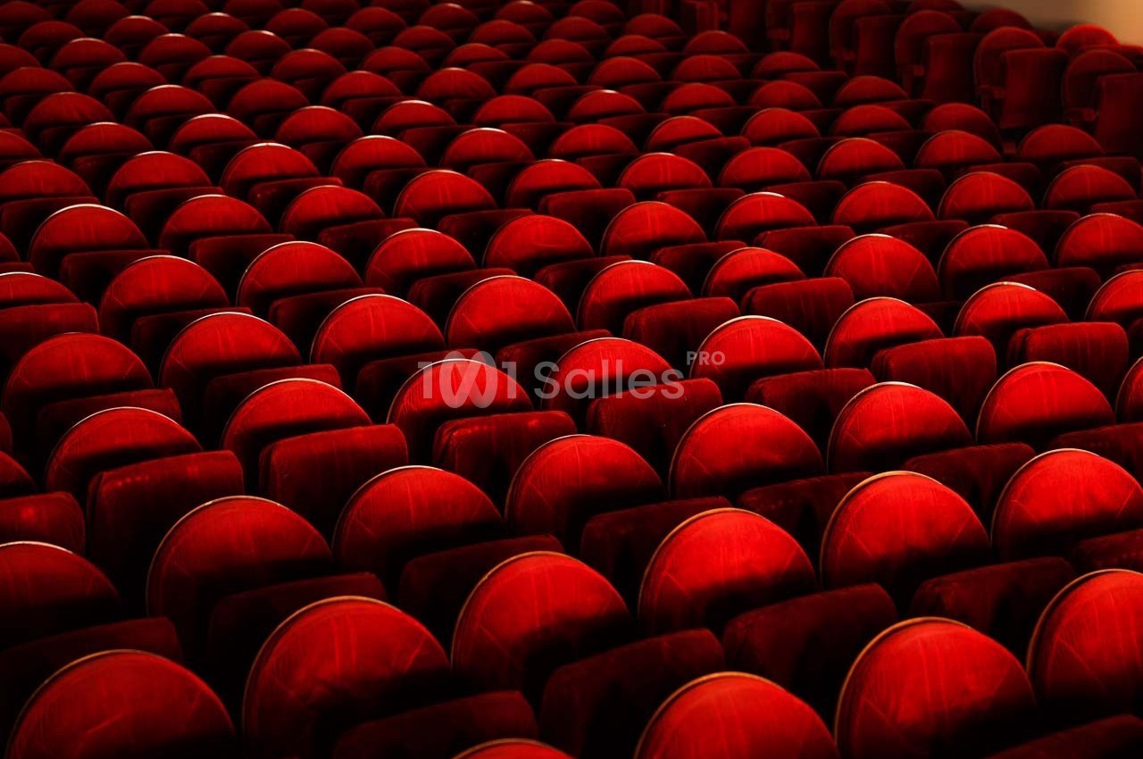 Rangées de sièges en velours rouge alignées dans une salle de spectacle vide.