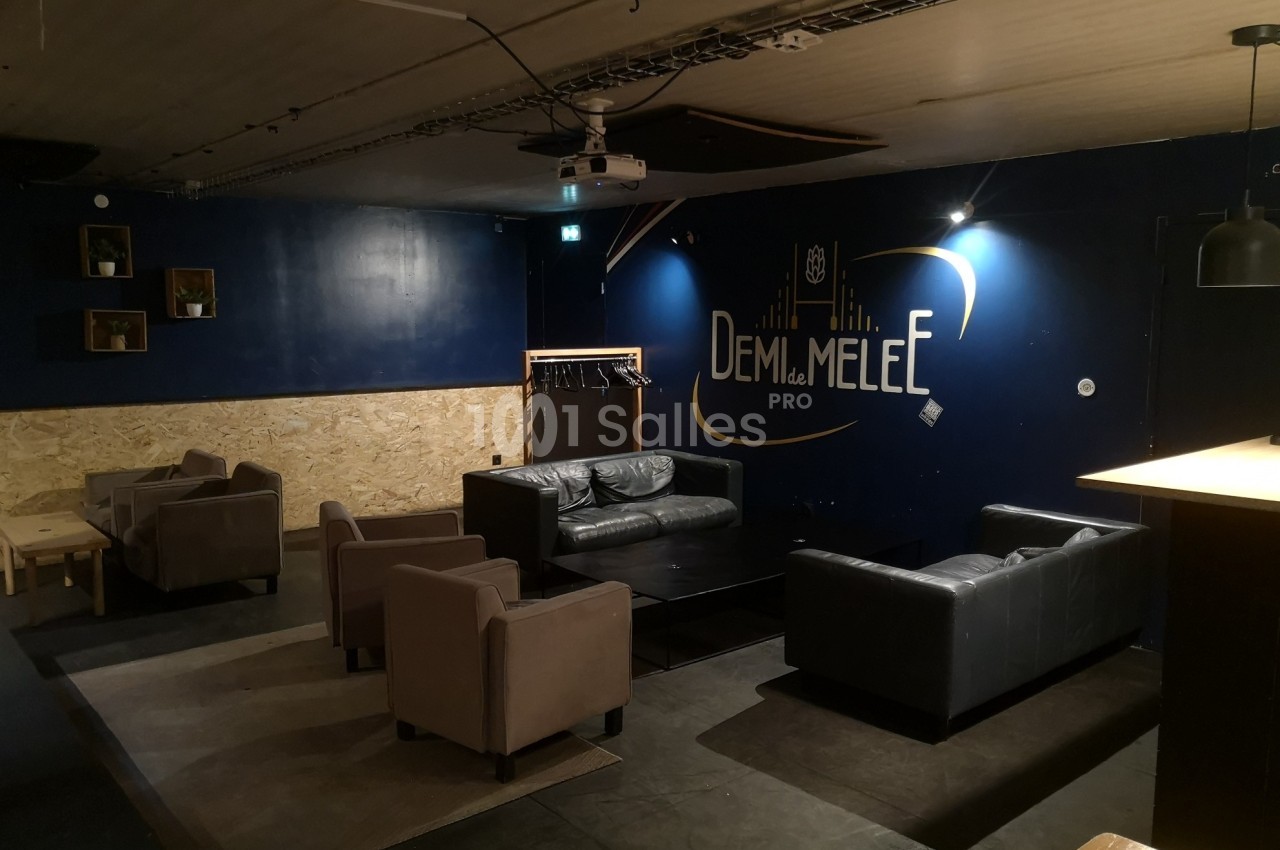 Espace lounge avec canapés et fauteuils disposés autour de tables basses, éclairage tamisé et mur bleu décoré.