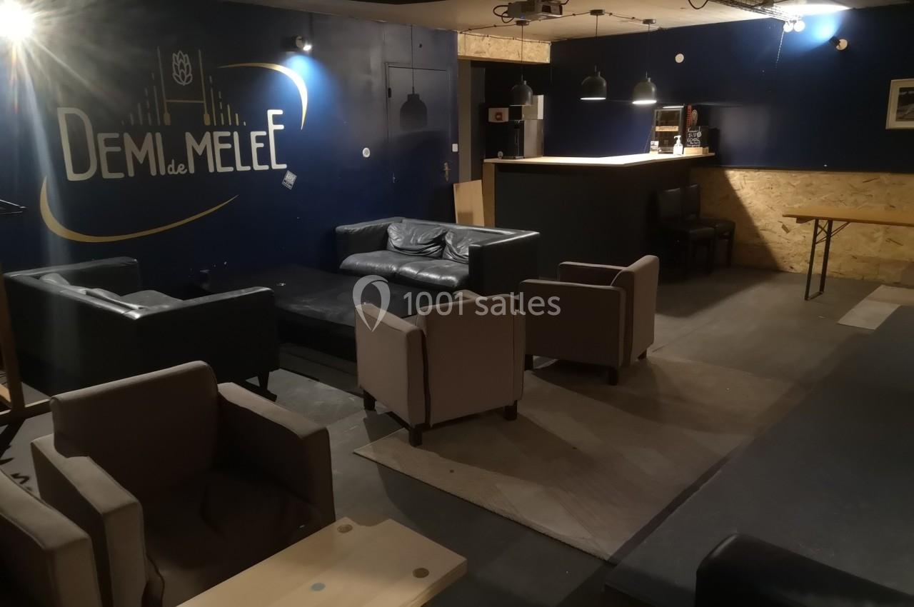 Espace intérieur avec fauteuils, canapé, bar et murs sombres, ambiance conviviale et éclairage tamisé.