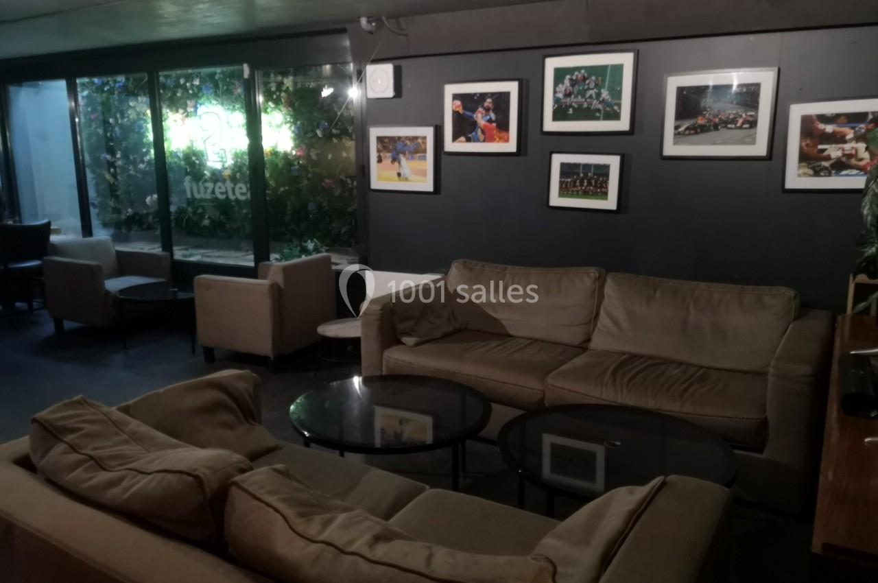 Espace salon avec canapés beiges, tables basses en verre, murs décorés de photos et grande baie vitrée donnant sur l…