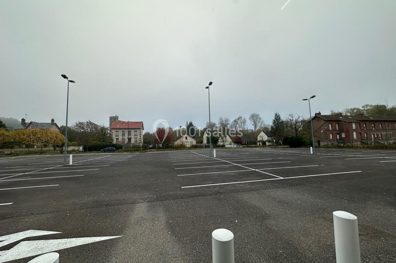 Parking vide avec marquages au sol, entouré de bâtiments résidentiels et d'arbres sous un ciel nuageux.