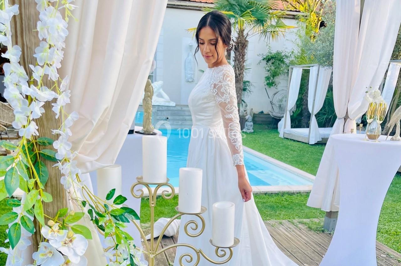 Une femme en robe de mariée blanche se tient près d'une piscine, entourée de décorations florales et de bougies.