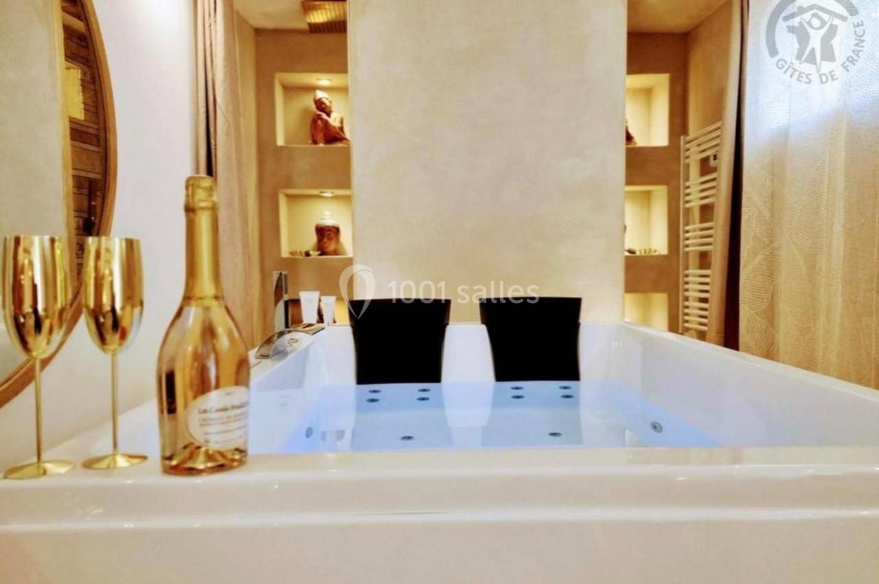 Baignoire balnéo remplie d'eau, entourée de deux flûtes dorées, une bouteille et une décoration murale chaleureuse.