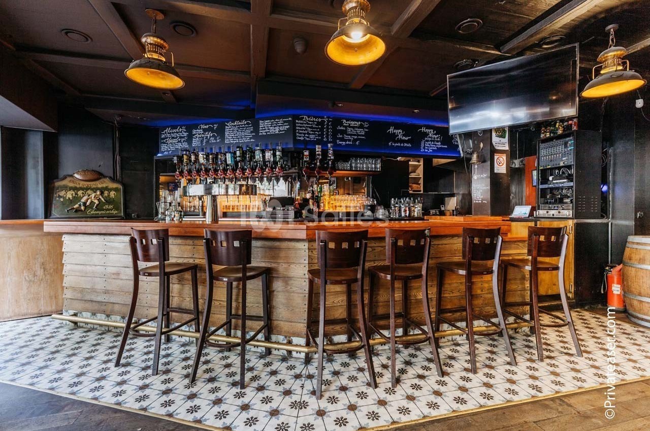 Bar en bois avec tabourets alignés, étagères de bouteilles et ardoises affichant des menus, éclairage chaleureux.