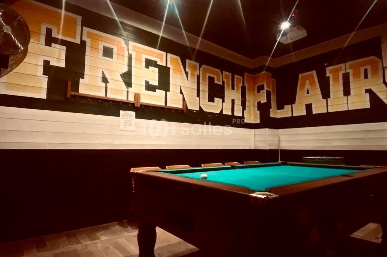 Table de billard dans une salle sombre avec des murs décorés du texte ’French Flair’ en grandes lettres.