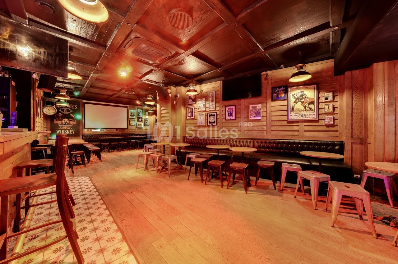 Intérieur d'un bar chaleureux avec des tables en bois, des tabourets et une décoration murale rétro.