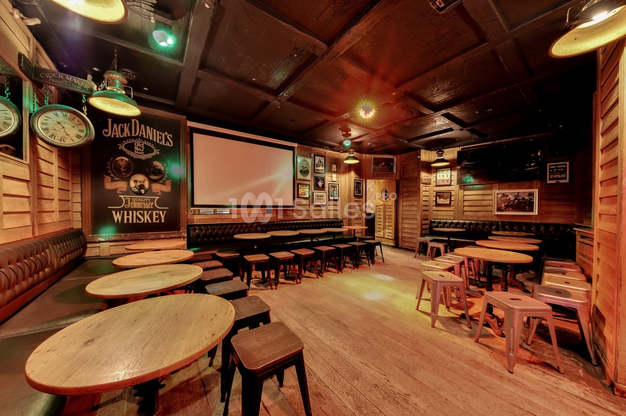 Salle de bar chaleureuse avec tables en bois, tabourets métalliques et décoration murale rétro sous un éclairage tamisé.