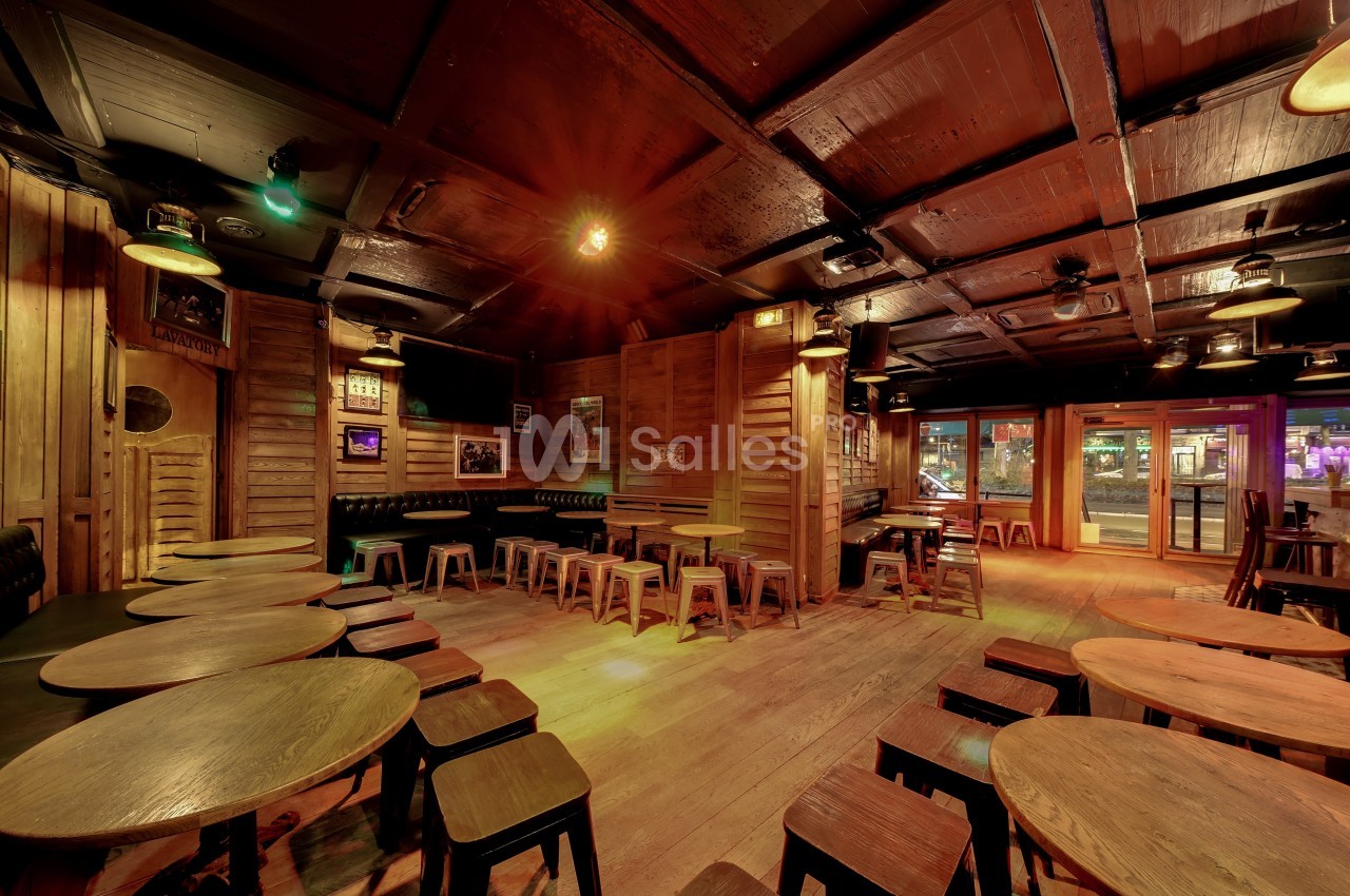 Intérieur d'un bar en bois avec des tables rondes, des tabourets et une lumière tamisée.