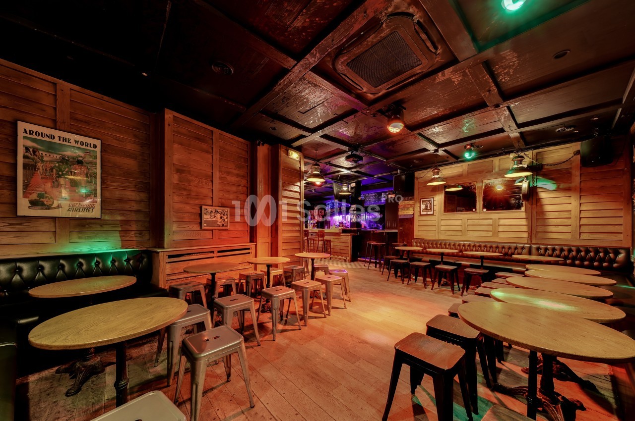Salle de bar en bois avec tables rondes, tabourets métalliques et éclairage tamisé, ambiance chaleureuse.