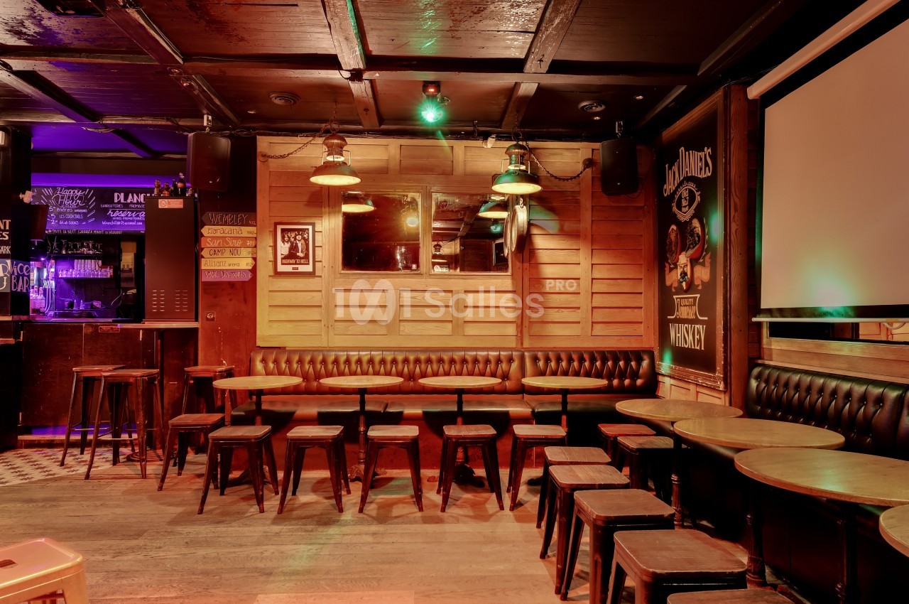 Salle de bar avec tables en bois, tabourets, banquettes en cuir et éclairage tamisé dans une ambiance chaleureuse.