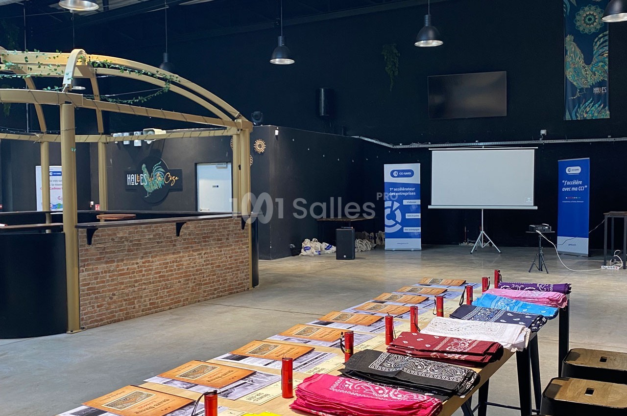 Salle aménagée avec des tables couvertes de brochures et de bandanas colorés, un écran de projection et des affiches en…