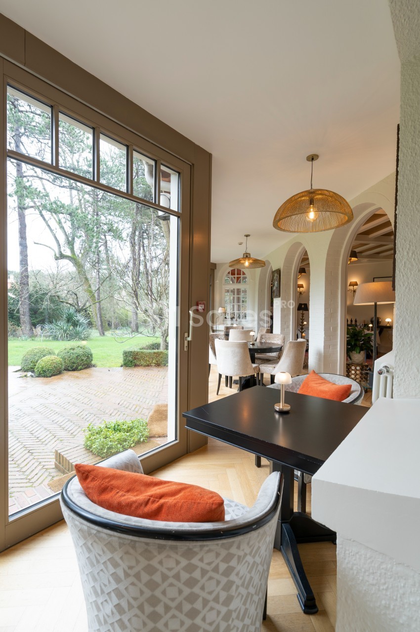 Salle à manger lumineuse avec grandes baies vitrées, vue sur un jardin, meubles élégants et décorations chaleureuses.