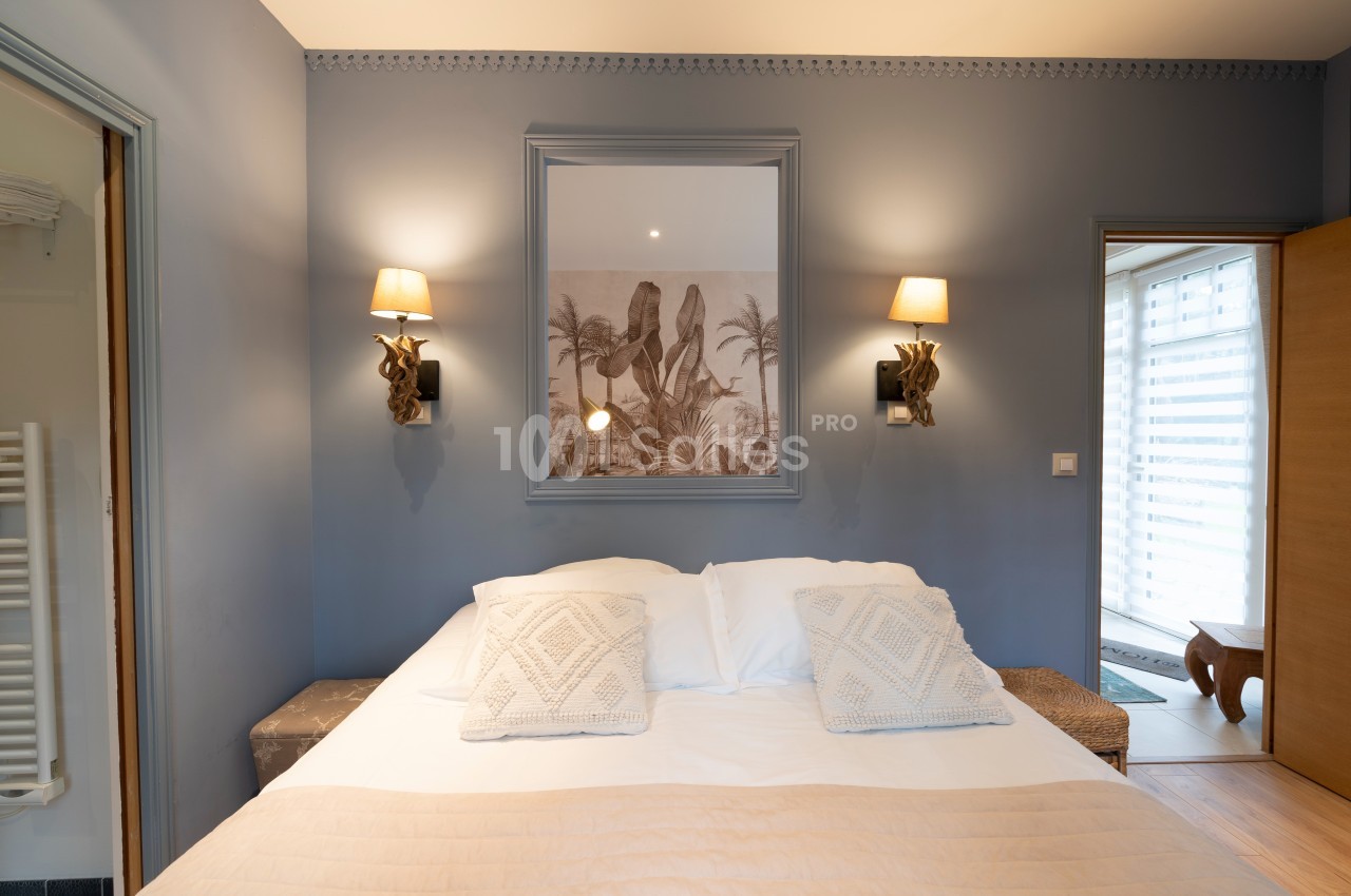 Chambre avec un lit double, murs bleus, éclairage mural et décoration murale représentant un paysage exotique.