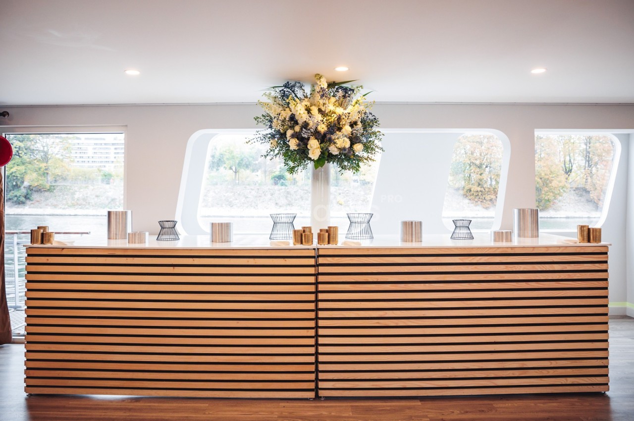Comptoir en bois clair décoré d'un grand bouquet de fleurs blanches et jaunes, dans un espace lumineux avec vue extérieure.