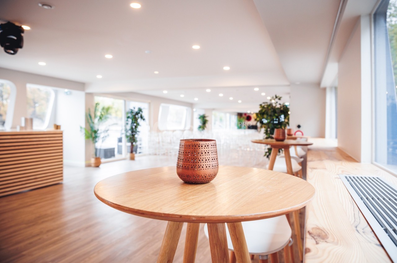 Salle lumineuse avec des tables en bois, une bougie décorative au premier plan et des plantes en arrière-plan.