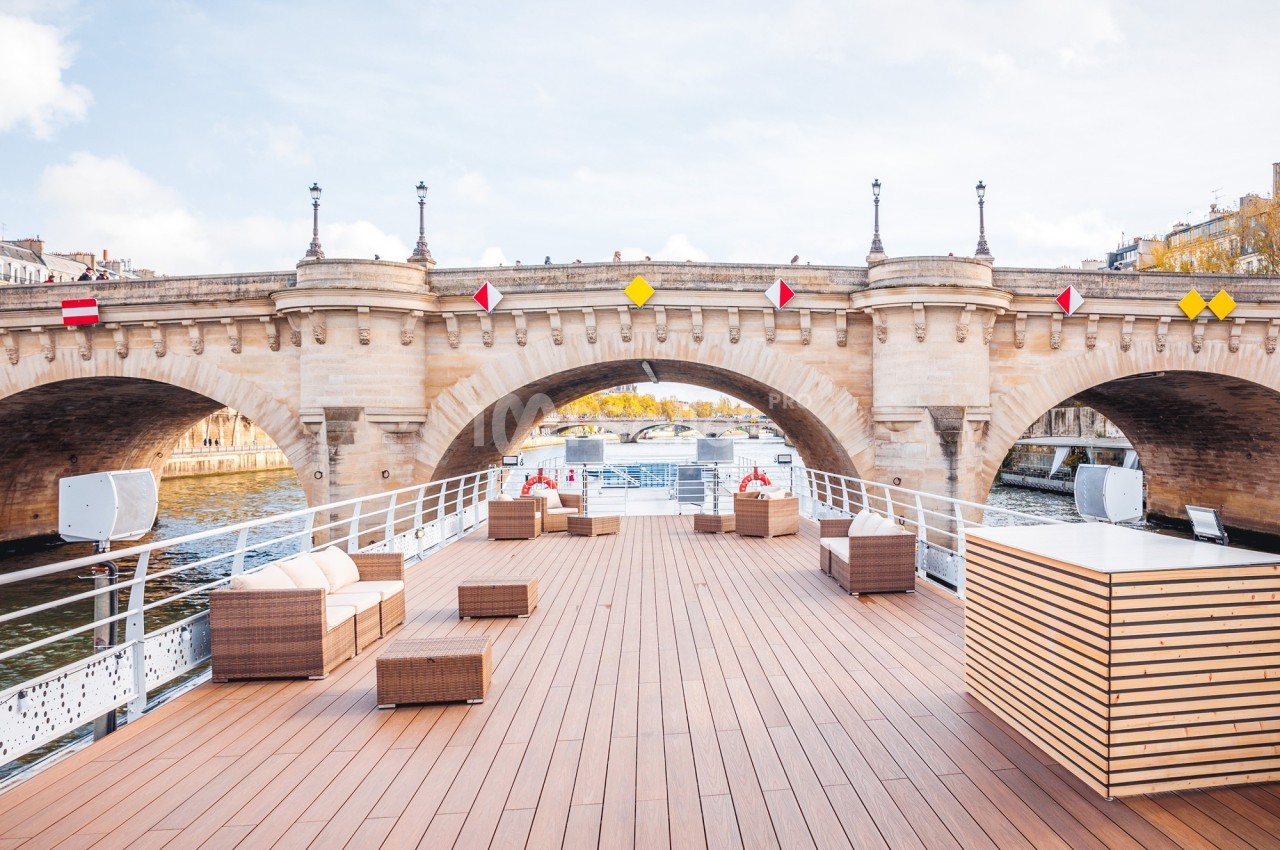 Pont en pierre traversant une rivière, vu depuis le ponton d'un bateau aménagé avec des meubles en rotin.
