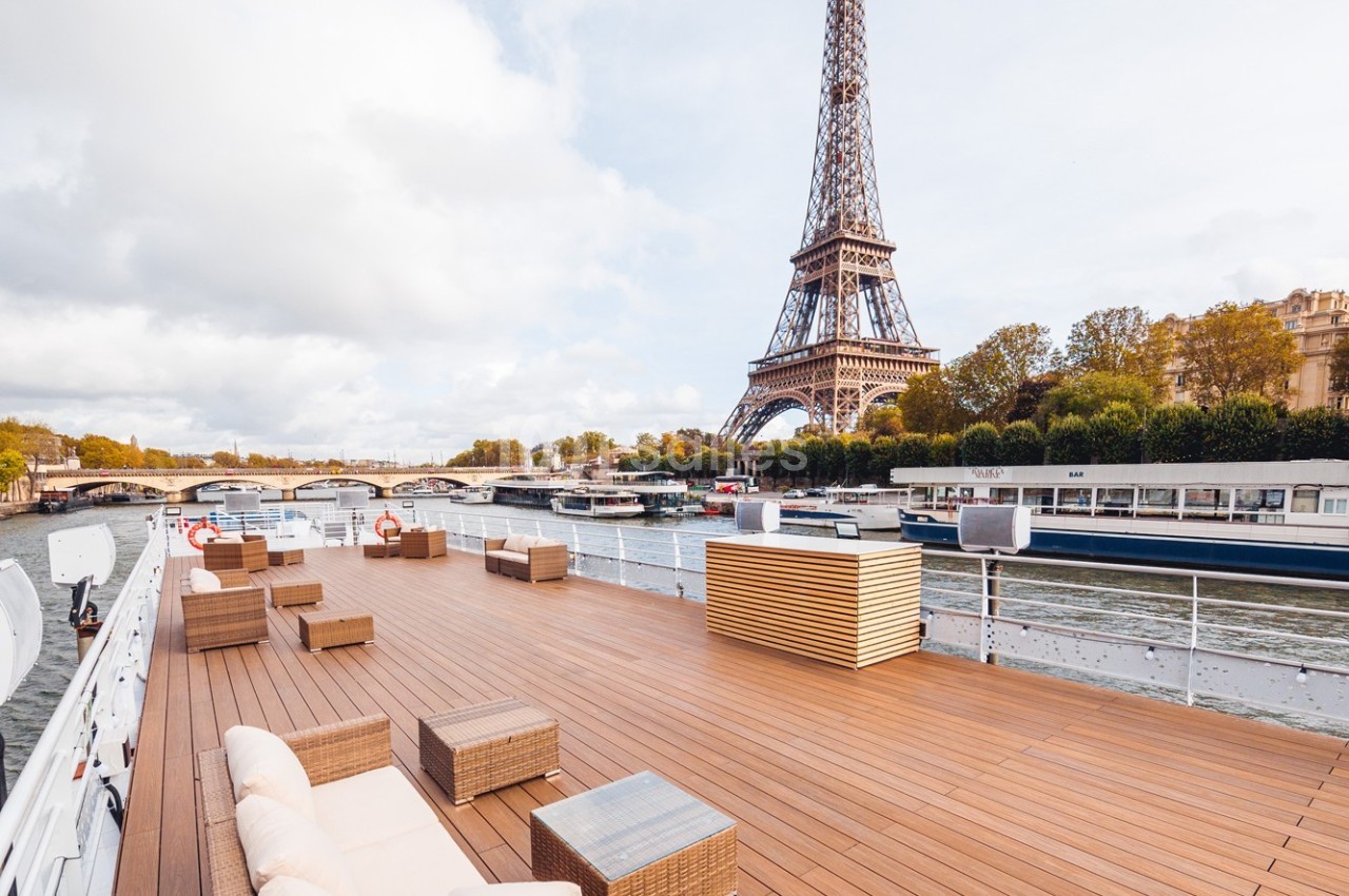 Terrasse en bois d'un bateau sur la Seine avec vue sur la tour Eiffel et les quais parisiens.