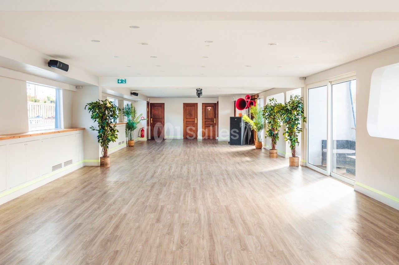 Salle lumineuse avec parquet, plantes en pot, grandes portes en bois et baies vitrées donnant sur l'extérieur.