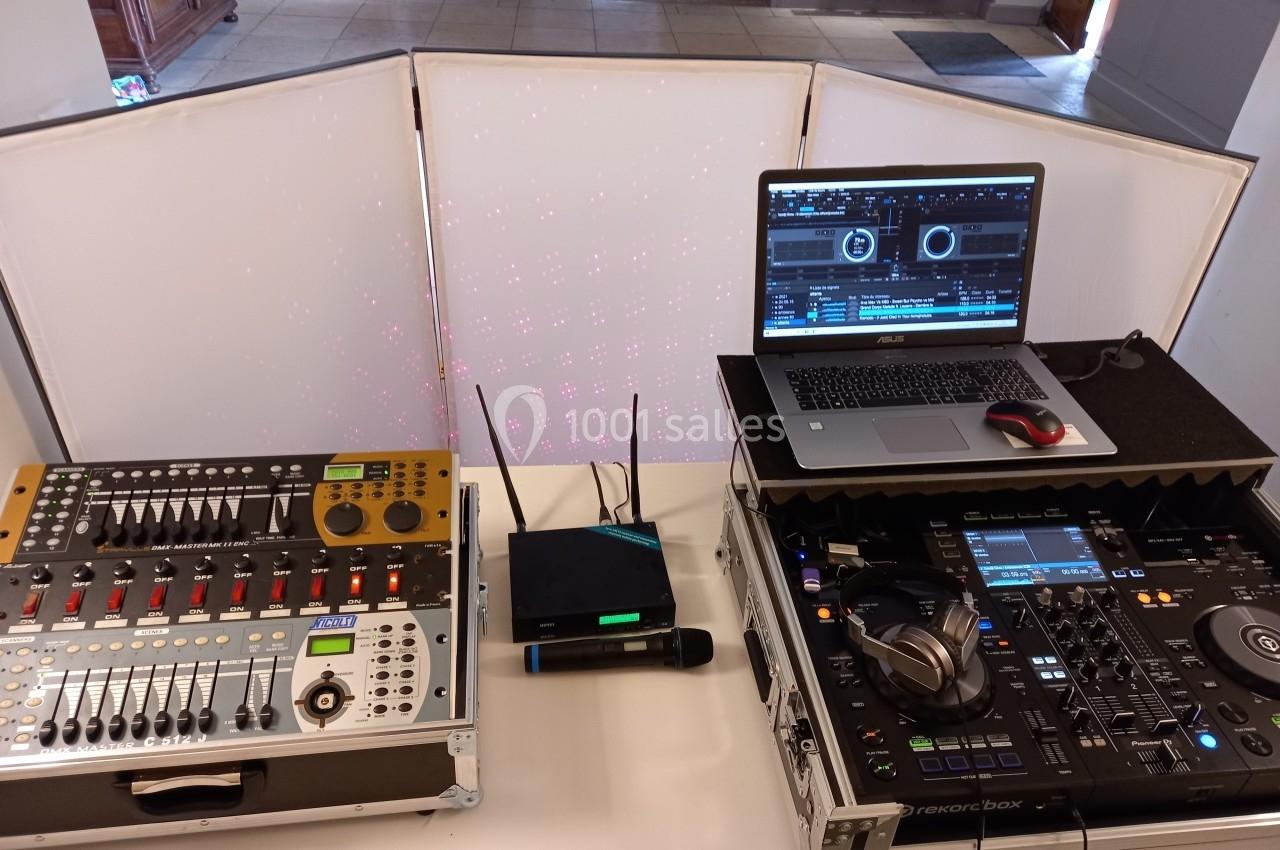 Équipement de DJ avec table de mixage, ordinateur portable, casque et micro sur une table dans une salle.