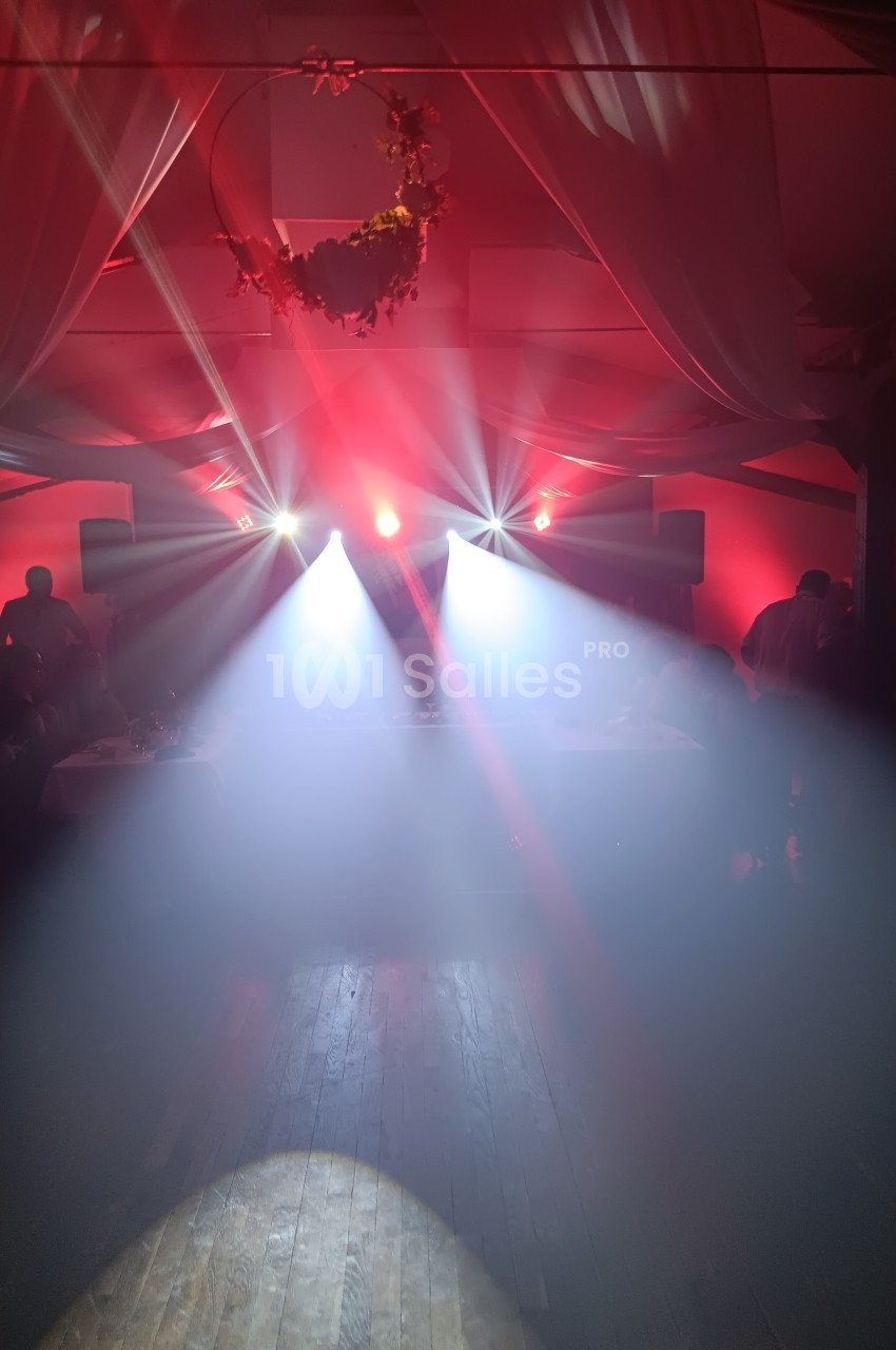 Salle de réception avec éclairage rouge et projecteurs lumineux diffusant de la fumée sur une piste en bois.