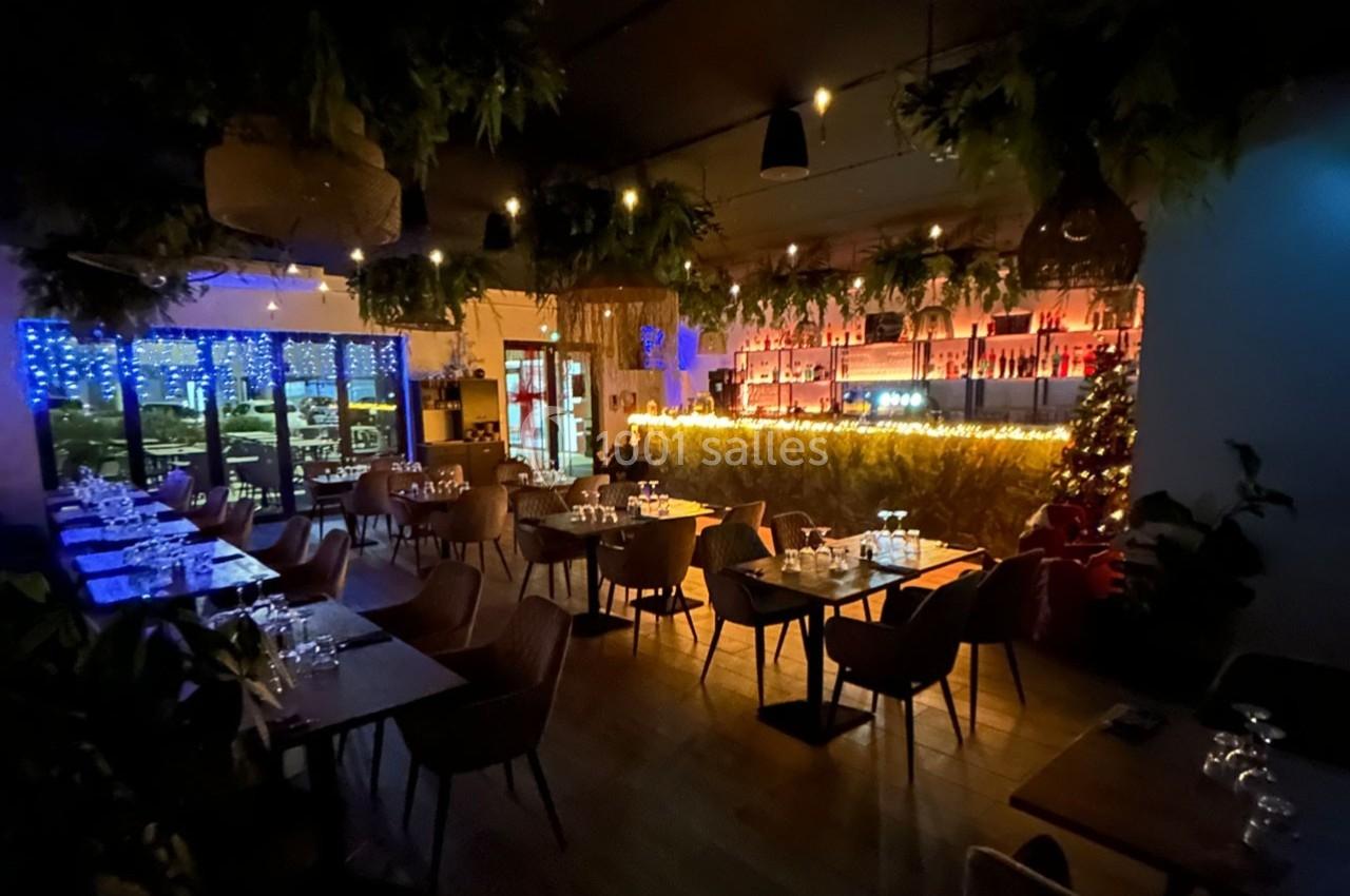Salle de restaurant chaleureuse avec éclairage tamisé, décor végétal et tables dressées.