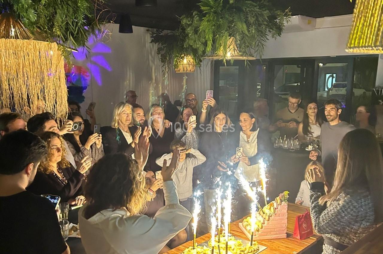 Un groupe de personnes célèbre un événement autour d'une table avec des desserts décorés de cierges magiques.