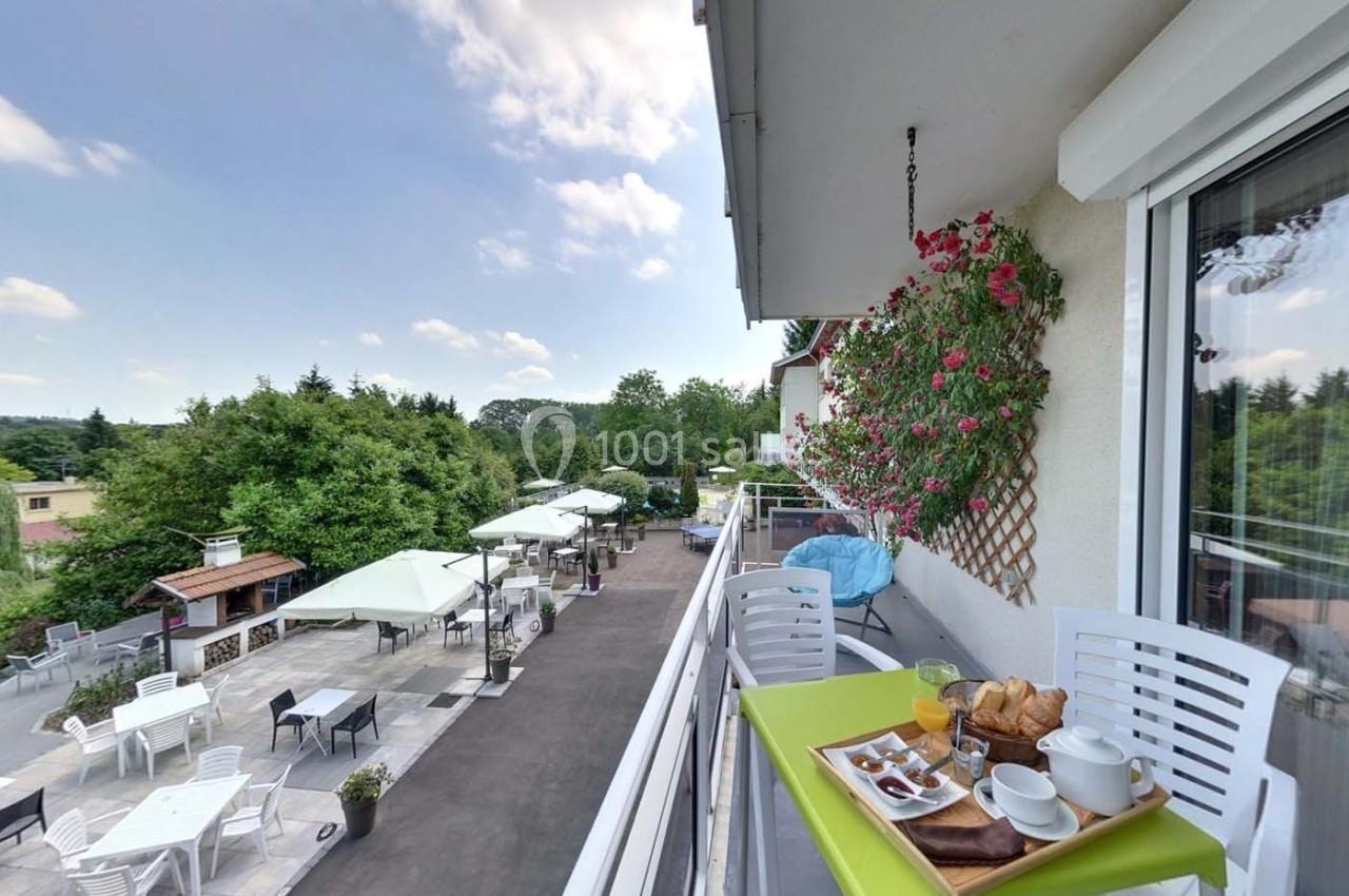 Petit-déjeuner servi sur un balcon avec vue sur une terrasse aménagée, des arbres et un ciel partiellement nuageux.