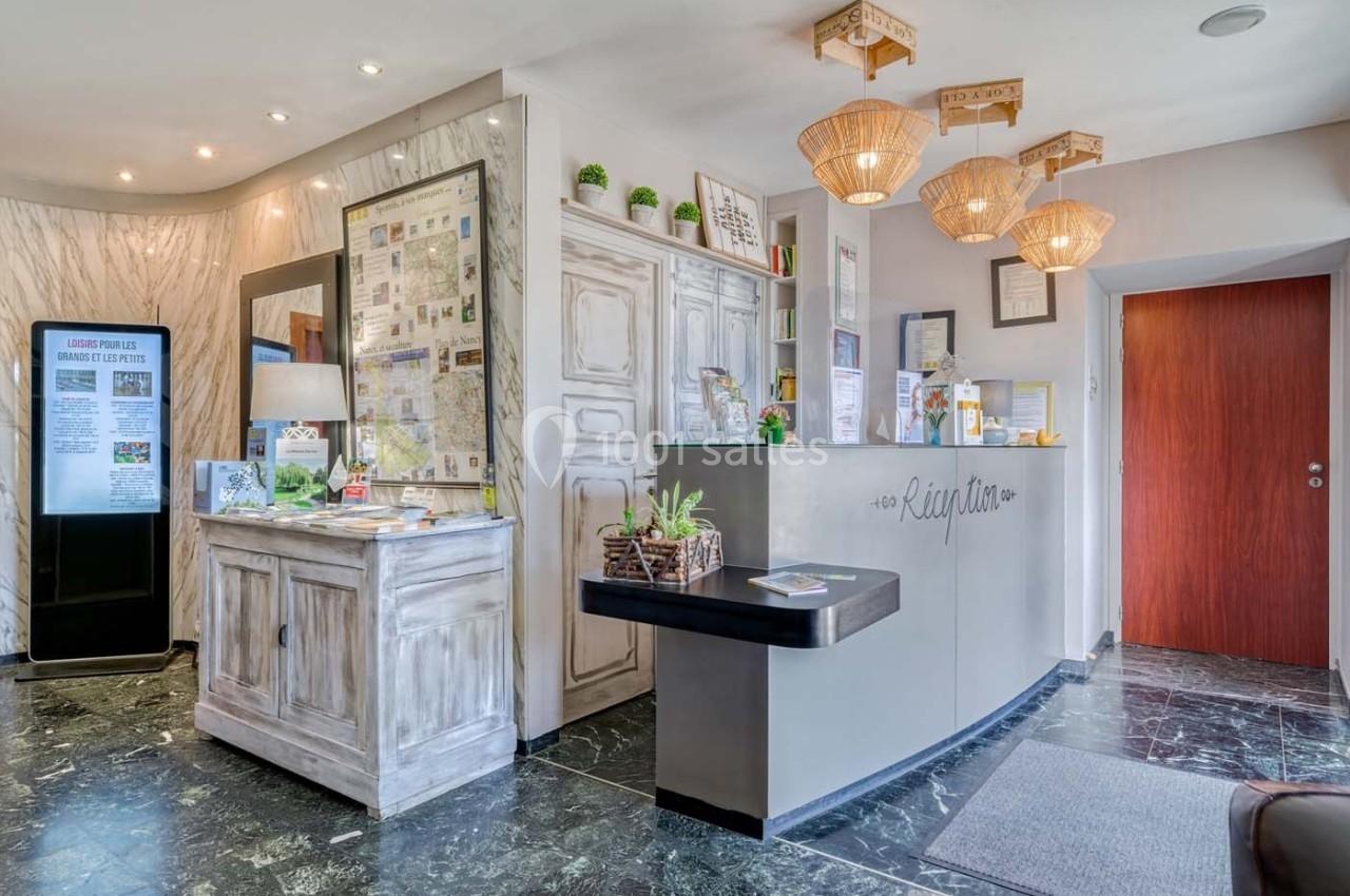 Réception d'un hôtel avec comptoir moderne, décorations végétales, éclairage chaleureux et présentoirs d'informations…