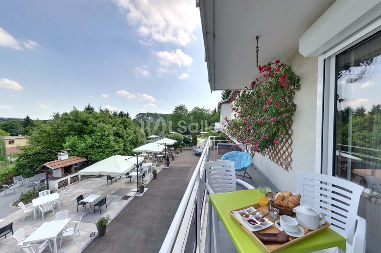 Petit-déjeuner servi sur un balcon avec vue sur une terrasse aménagée, des parasols et un paysage verdoyant.