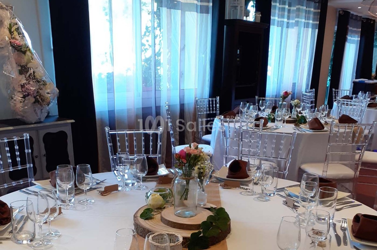 Salle de réception décorée avec des tables rondes dressées, nappes blanches et centres de table floraux.