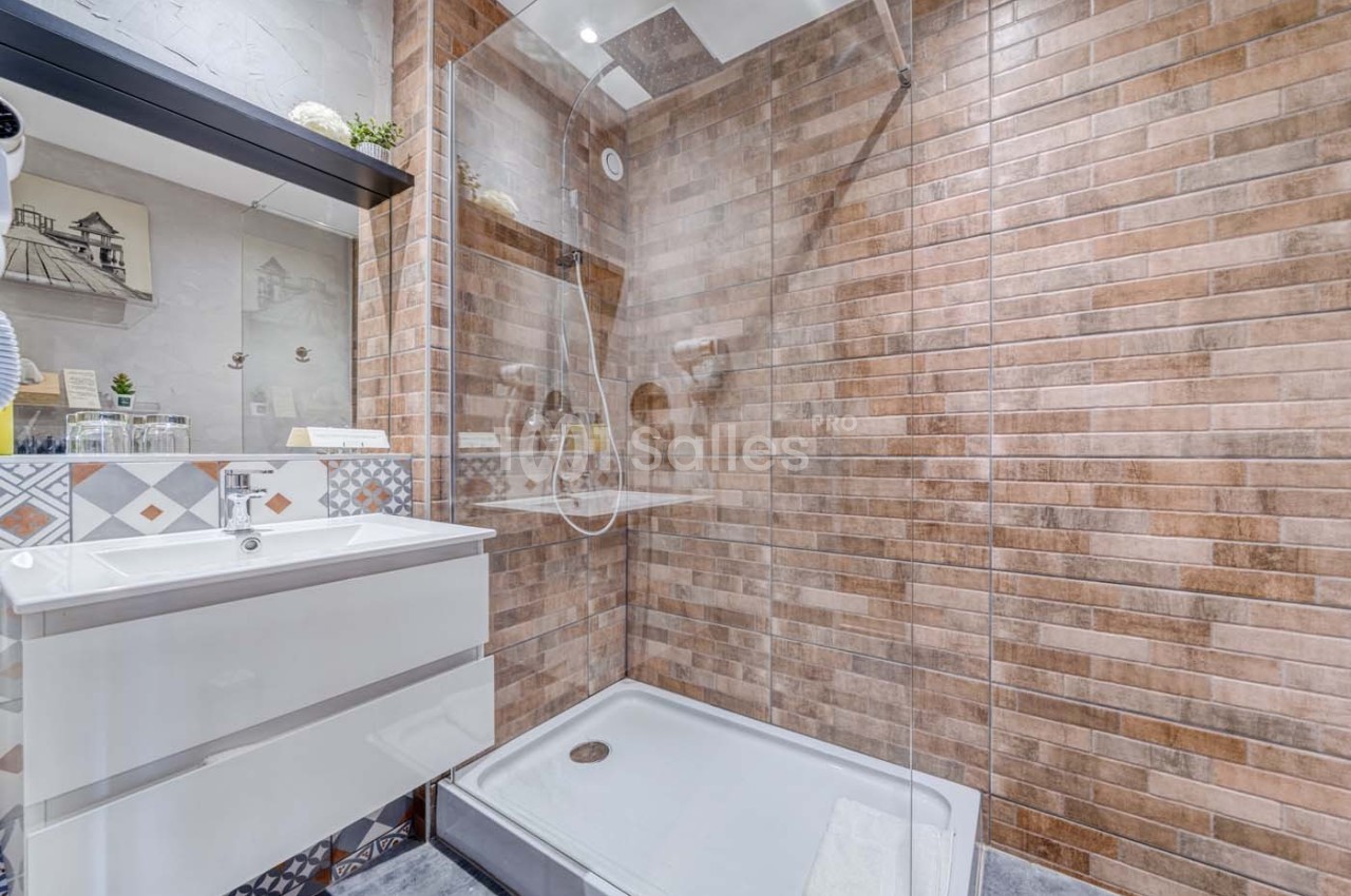 Salle de bain moderne avec douche à l'italienne, carrelage mural effet briques et meuble lavabo blanc.