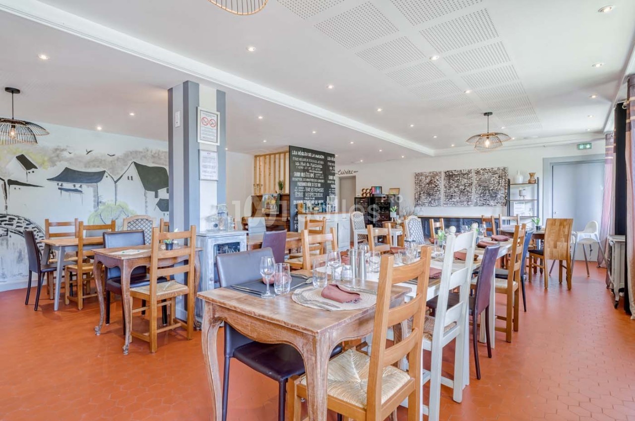 Salle de restaurant lumineuse avec tables en bois, chaises variées et décoration murale sobre.