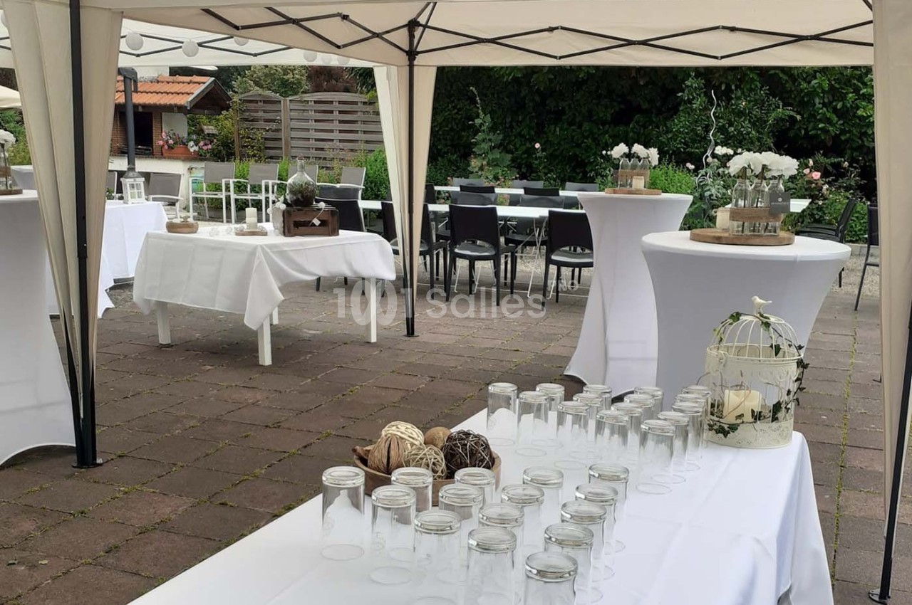 Tables décorées sous des tonnelles blanches dans un jardin, préparées pour un événement en extérieur.